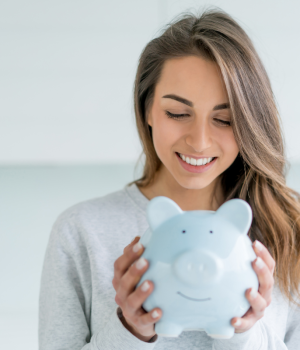 Smiling woman holding a light-blue piggy bank, symbolizing financial wellness.