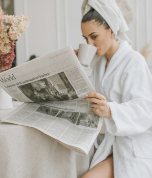 Woman in a white robe reading a newspaper and sipping coffee, symbolizing personal growth and learning.