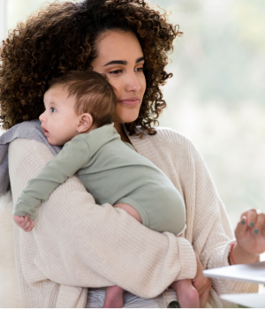 Woman holding her baby while working on a laptop, balancing work and home life.