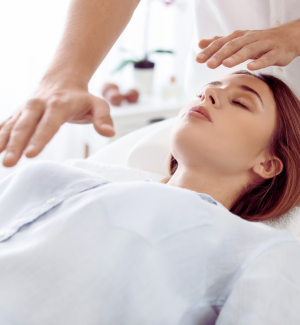Close-up of a woman receiving energy healing with a practitioner’s hands hovering over her forehead.