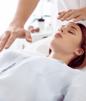 Close-up of a woman receiving energy healing with a practitioner’s hands hovering over her forehead.