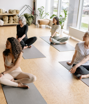 Diverse group of people on yoga mats performing seated stretches in a bright studio, symbolizing physical health.